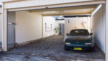 A car parked inside a garage with a white exterior, a brick floor, and a small plant in the corner.