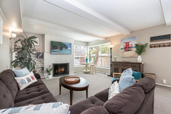 A living room with a fireplace, a large window, and a view of the outdoors.