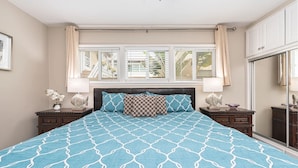 Quarto com uma cama grande, duas mesas de cabeceira, uma janela com persianas e vista para o exterior.