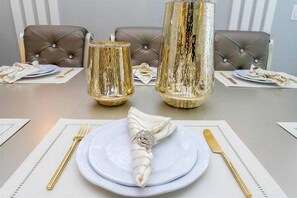 Una mesa de comedor dispuesta con platos, cubiertos y servilletas, con dos jarrones decorativos al fondo.