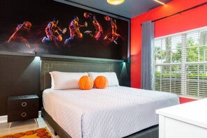 A modern hotel room with a large bed, a headboard with a basketball-themed artwork, and a window with blinds.