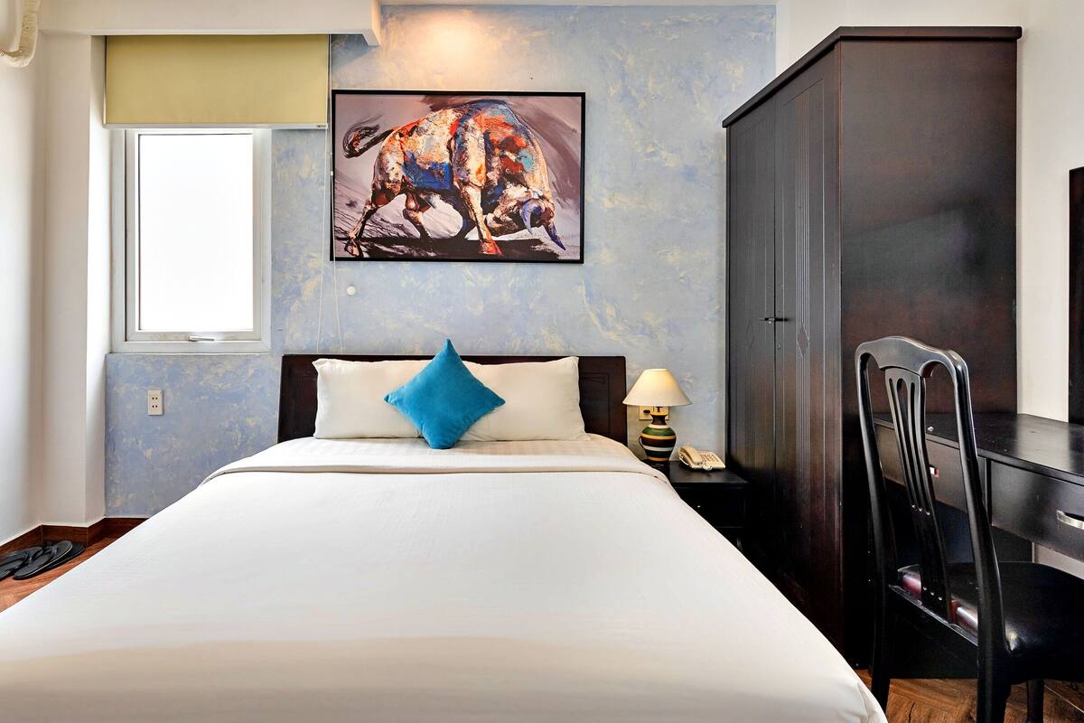Ein Hotelzimmer mit einem großen Bett, einem Schreibtisch, einem Sessel, einem Bild an der Wand und einem Fenster.