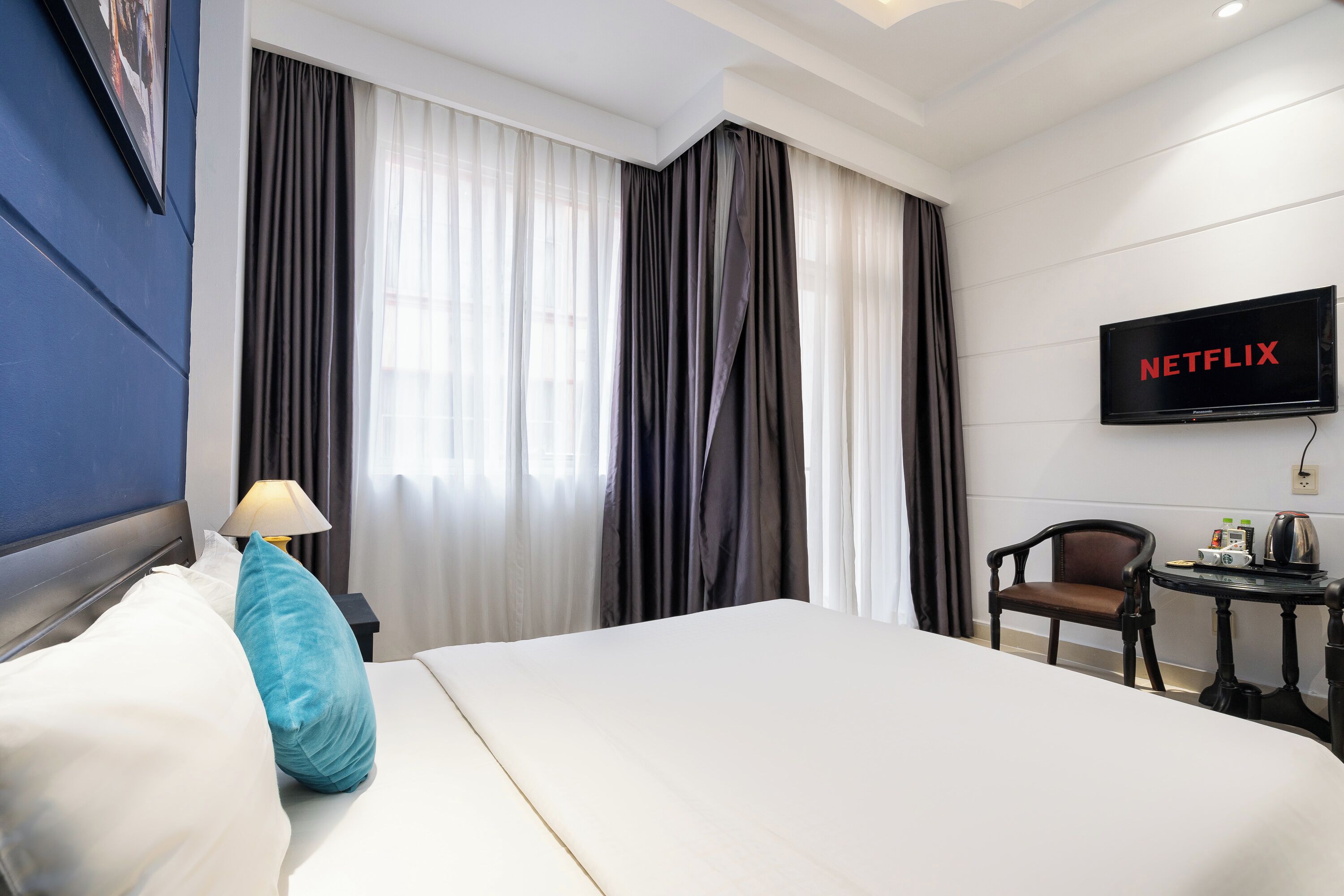 Une chambre d’hôtel avec un grand lit, un téléviseur fixé au mur, une chaise et une petite table avec une lampe.