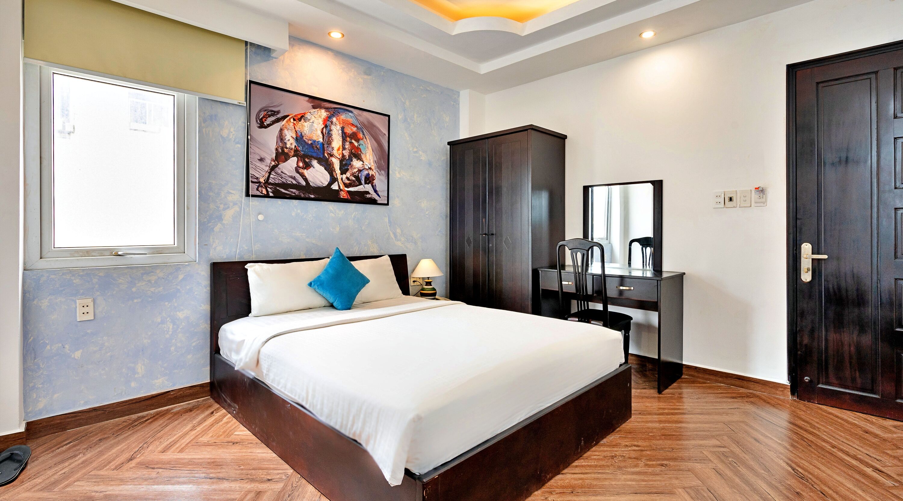 A hotel room with a large bed, a desk with a chair, a wardrobe, and a mirror.