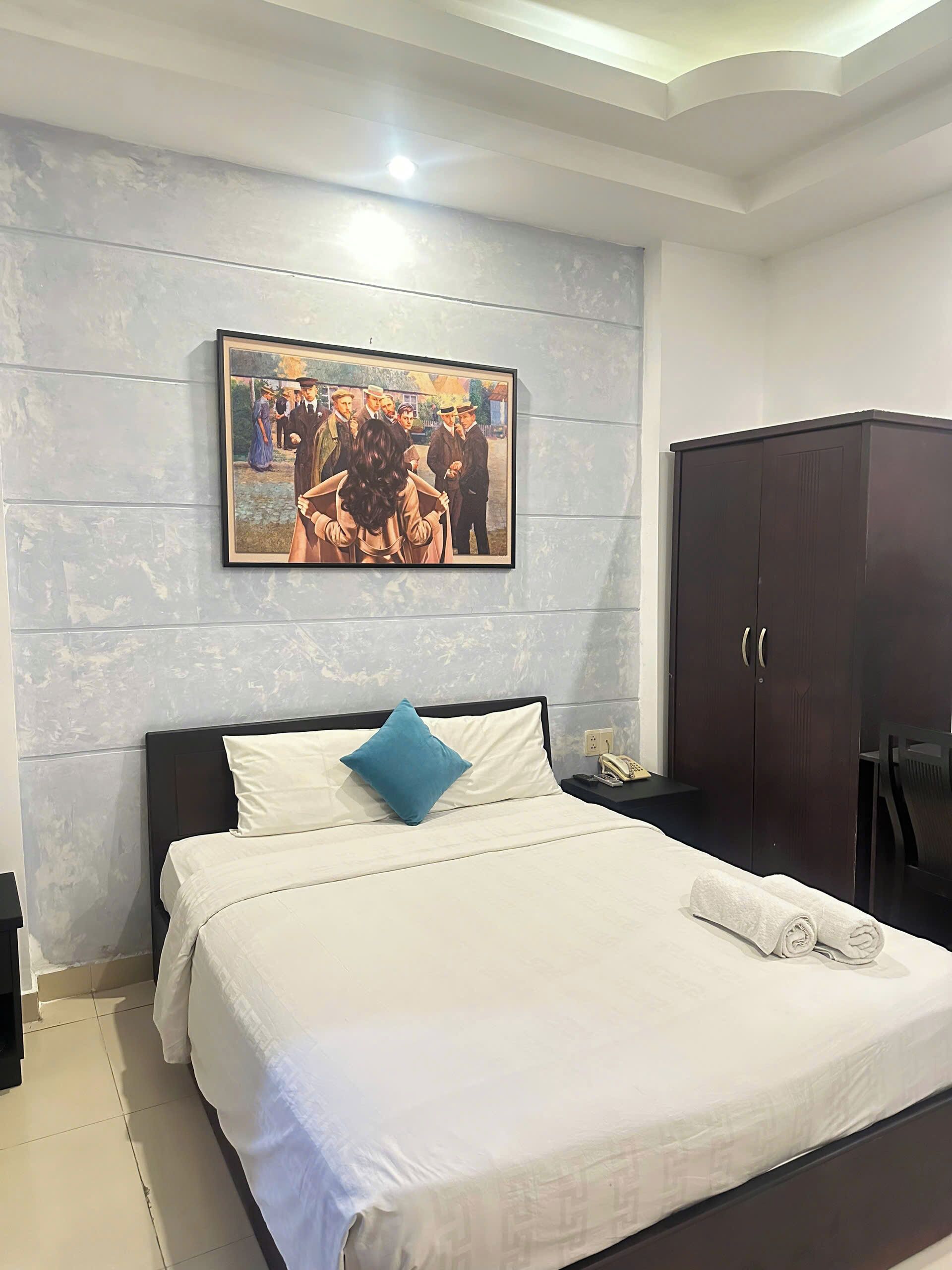Ein Hotelzimmer mit Bett, Nachttisch, Kleiderschrank und einem Gemälde an der Wand.