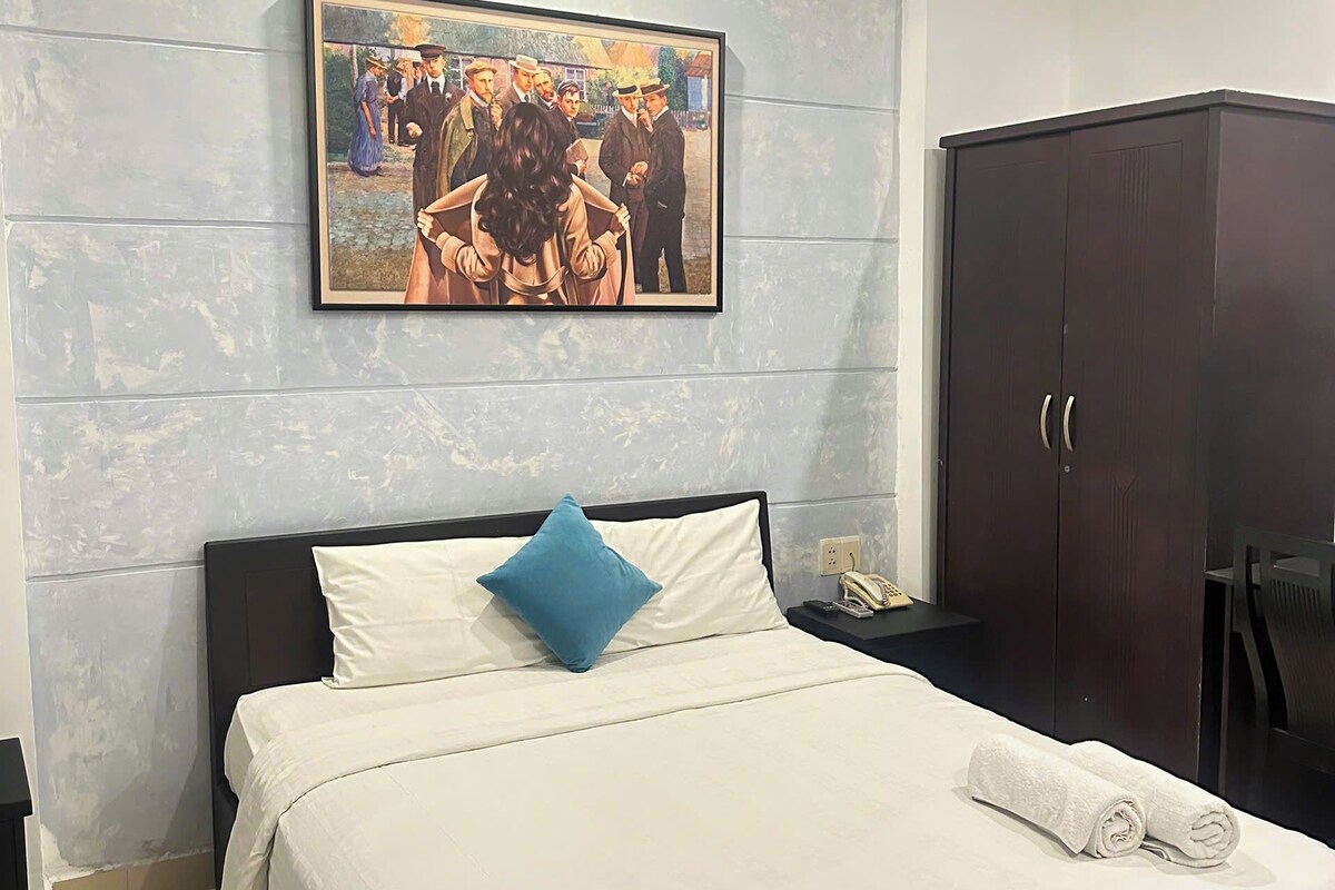 A hotel room with a bed, a nightstand, a wardrobe, and a painting on the wall.