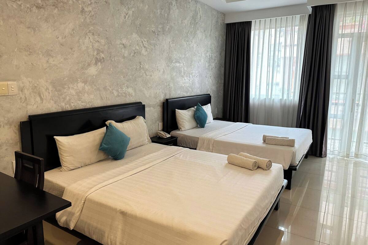 Ein Hotelzimmer mit zwei Betten, einem großen Fenster mit Vorhängen und einer strukturierten Wand.