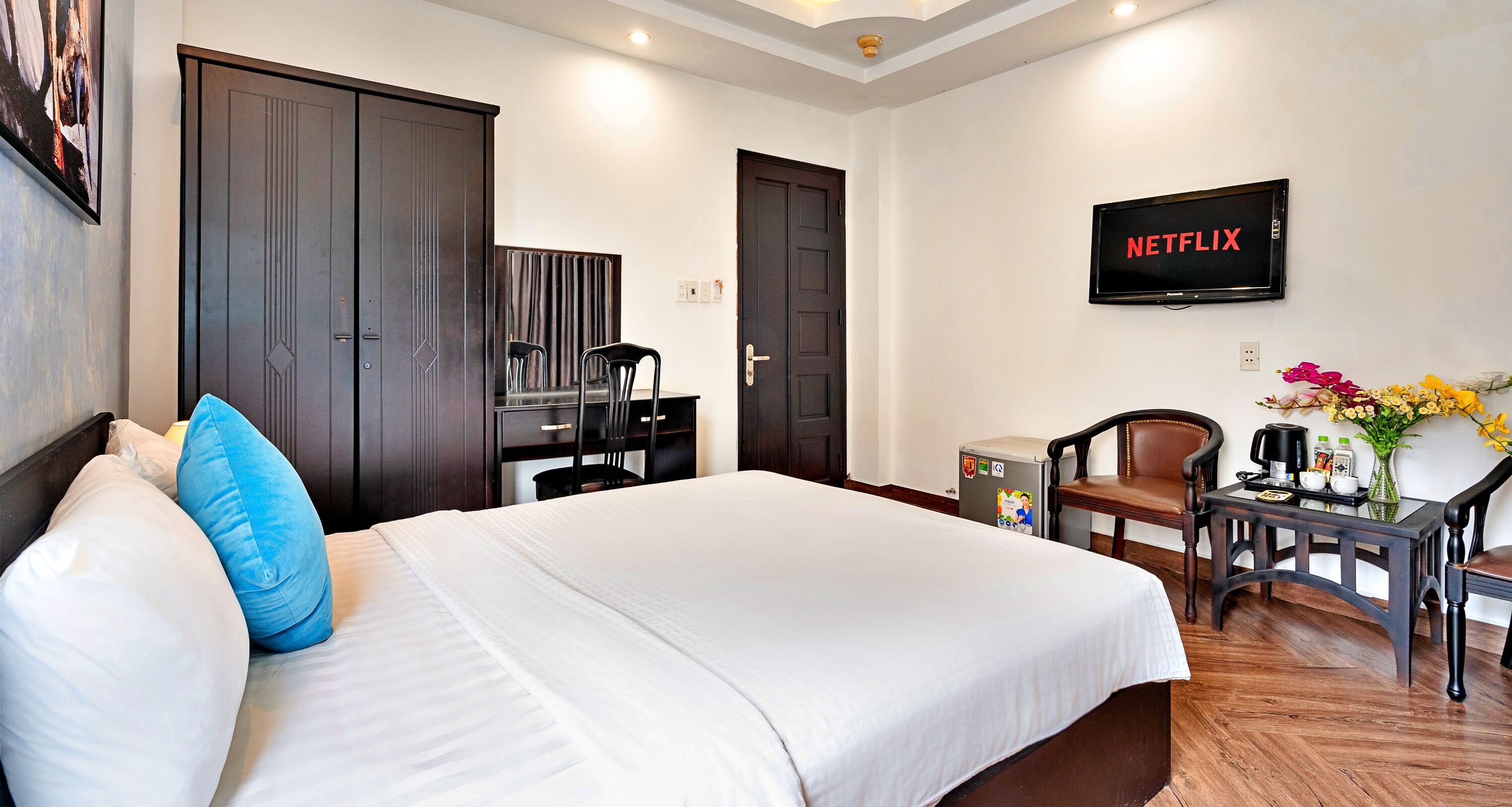 Une chambre d’hôtel équipée d’un lit, d’un bureau avec une chaise, d’un petit réfrigérateur et d’un téléviseur affichant le logo « NETFLIX ».