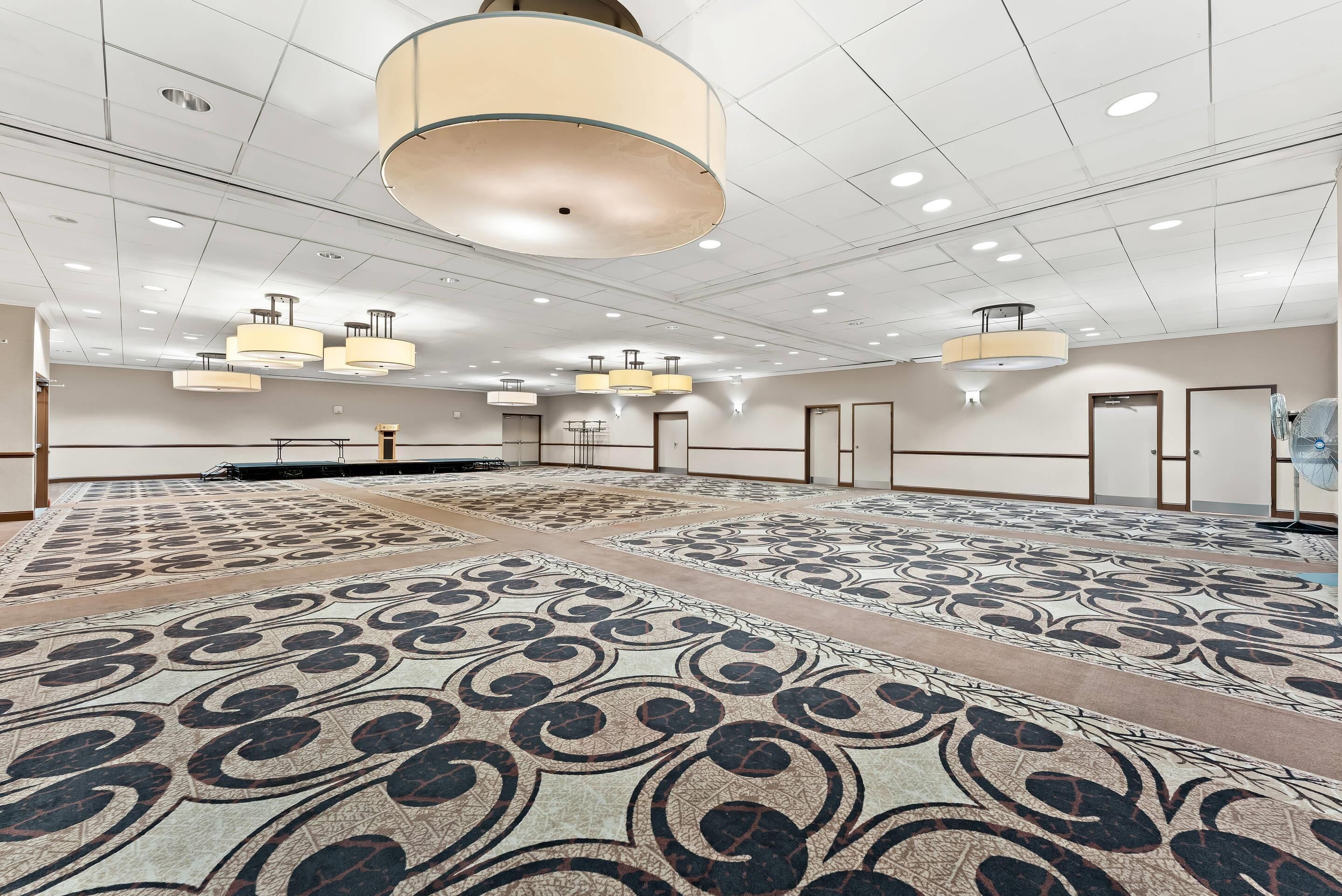 A spacious hotel room with a patterned carpet, multiple ceiling lights, and a large chandelier.