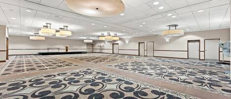 A spacious hotel room with a patterned carpet, multiple ceiling lights, and a large chandelier.