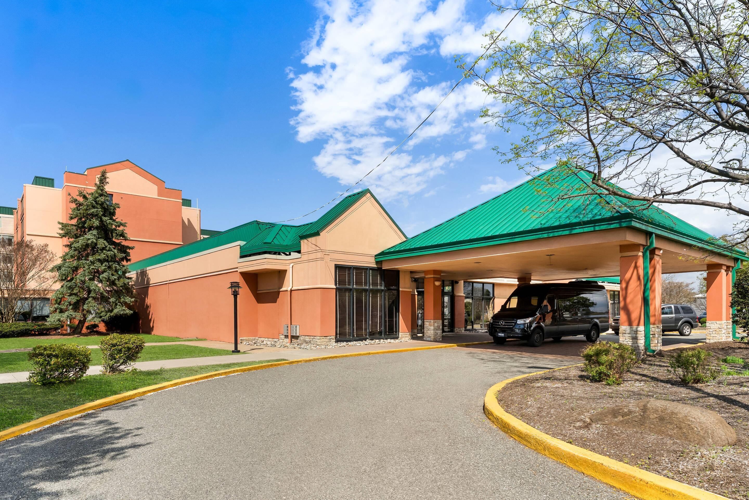 A hotel entrance with a green roof, a covered parking area, and a parking lot.