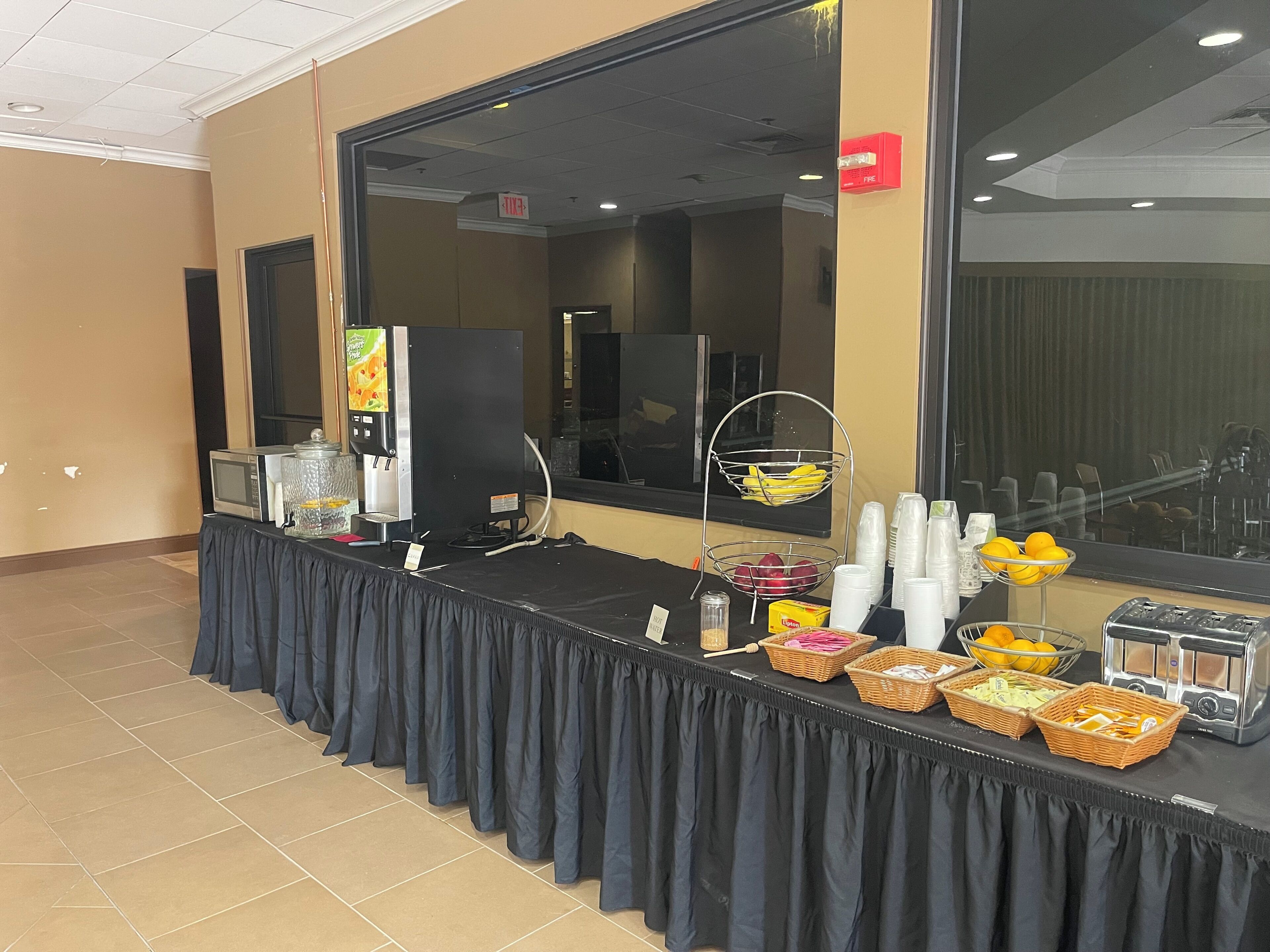 A buffet setup with a microwave, beverage dispenser, and various food items.