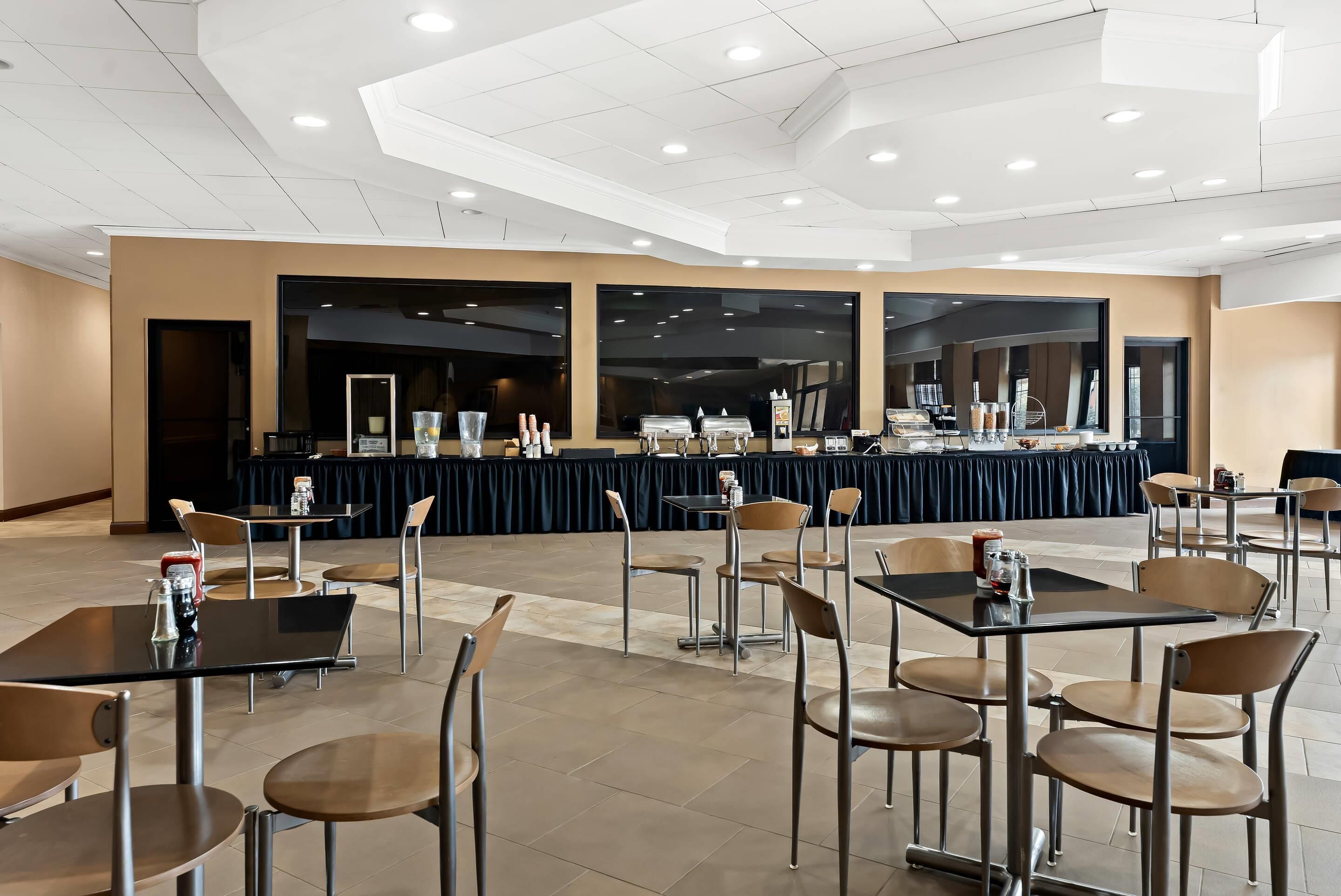 A spacious indoor dining area with multiple tables and chairs, a buffet setup in the background, and a modern ceiling design.