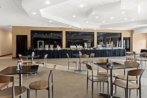 Een ruime, overdekte eetruimte met meerdere tafels en stoelen, een buffet in de achtergrond, en een modern plafondontwerp.