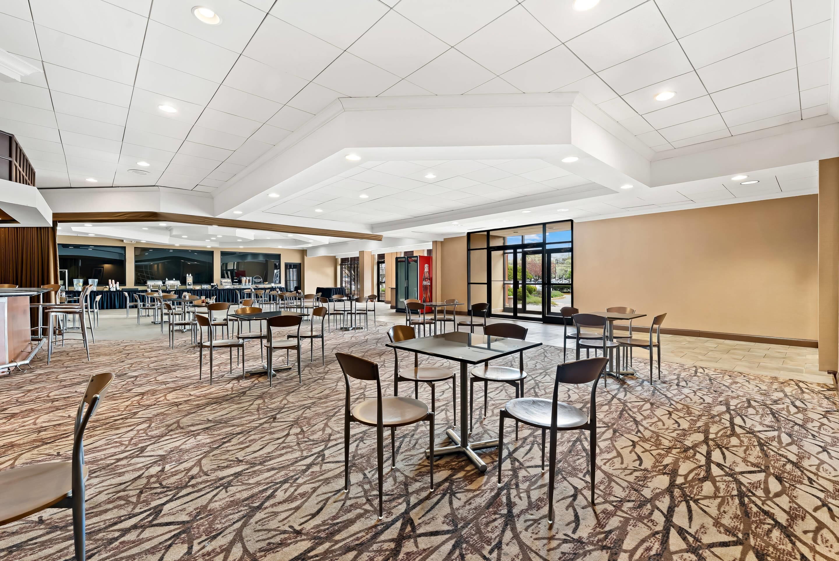 A spacious hotel lobby with multiple seating areas, a central counter, and large windows offering a view of the outdoors.