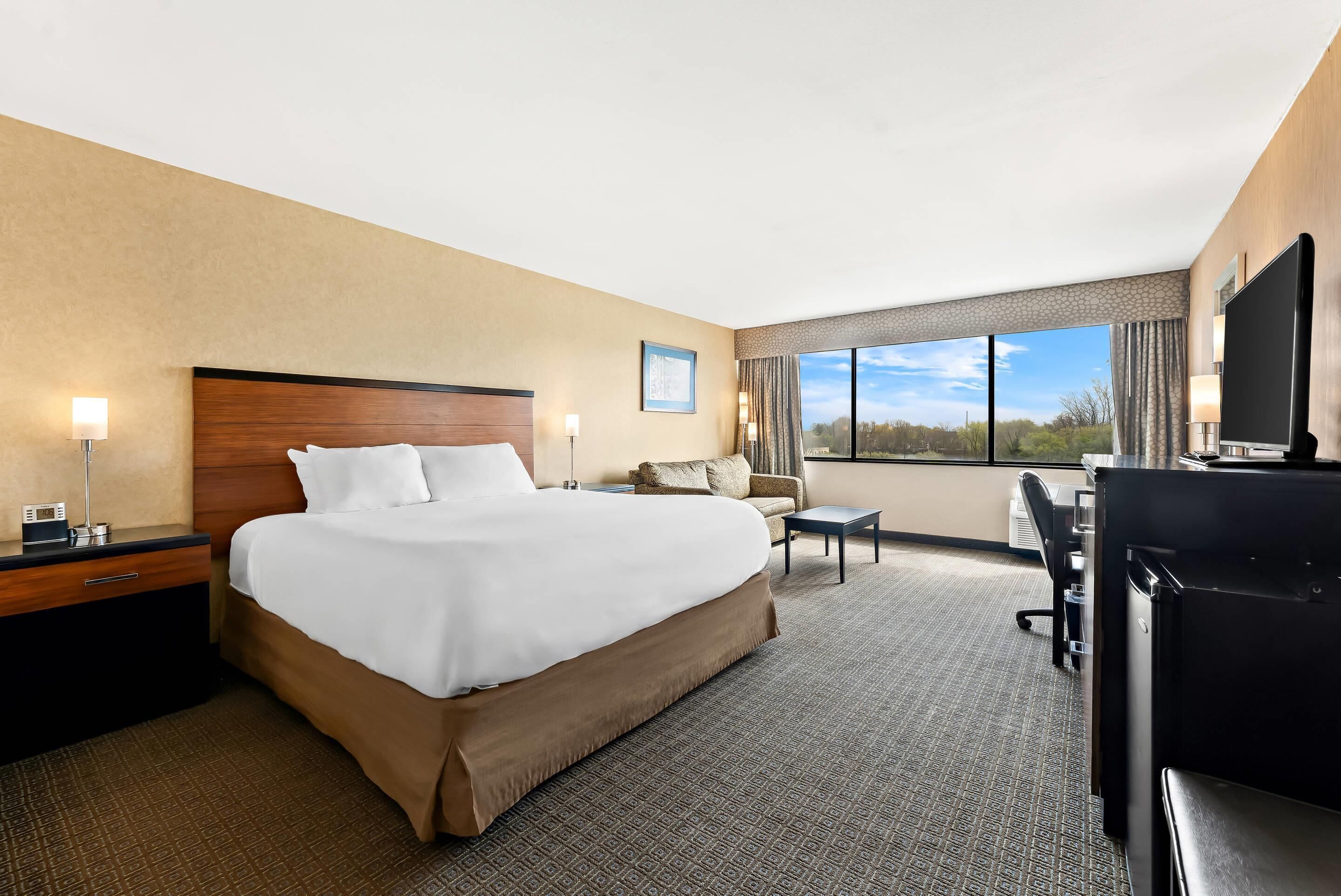 A hotel room with a large bed, a desk, a chair, and a TV.