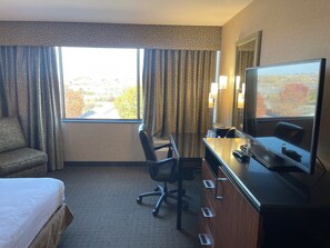 Relax in this inviting room with a large bed, desk, and TV, offering a peaceful view of the surrounding trees.