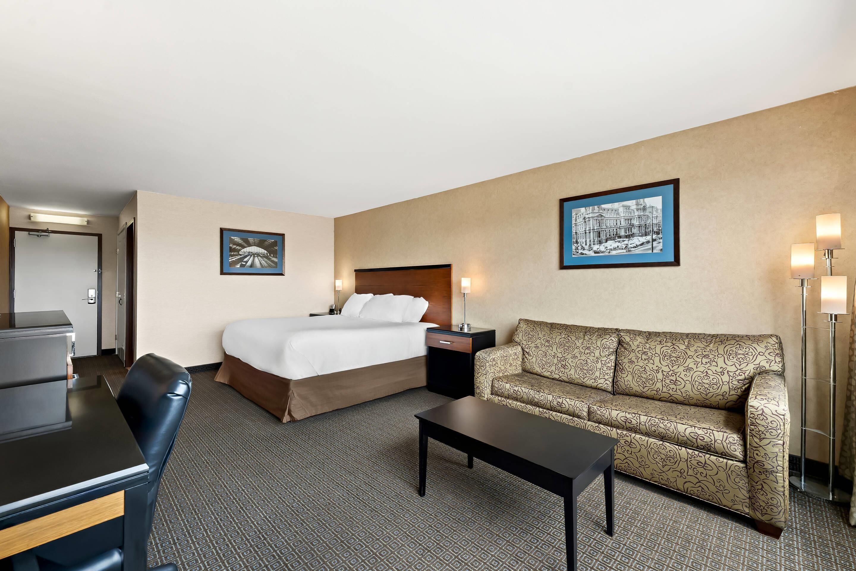 A hotel room with a bed, a sofa, a desk, and a lamp.