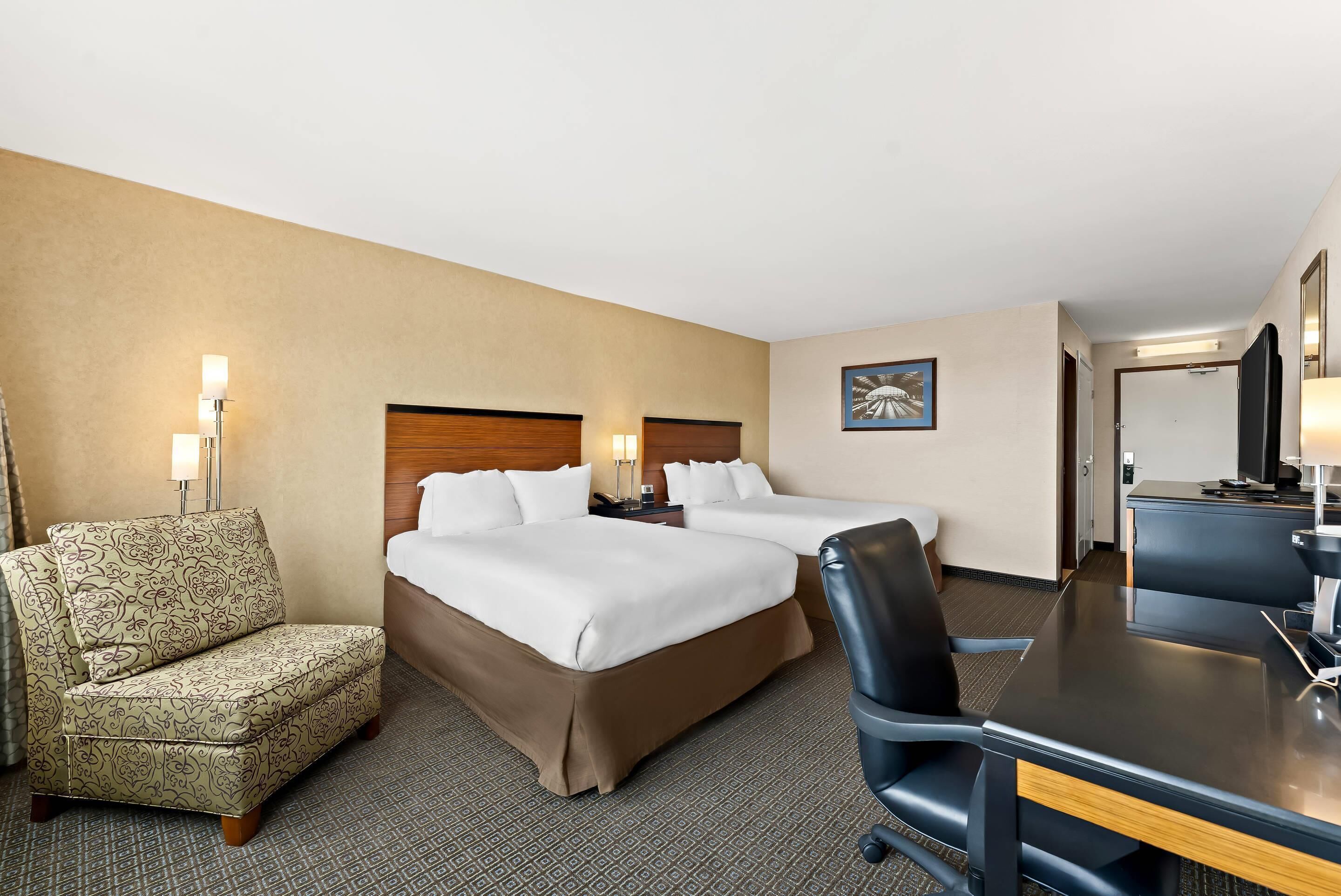 A hotel room with two beds, a desk, a chair, and a sofa.