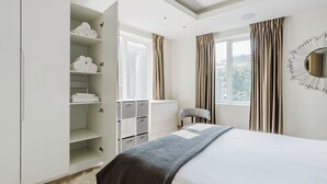 A bedroom with a bed, a wardrobe with shelves, a chair, and a window with curtains. - Chic St. John's Wood 1BR w/ Elevator, Fully Furnished, by Blueground (London)