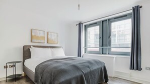 Een moderne slaapkamer met een groot bed, een klein nachtkastje en een raam met gordijnen.