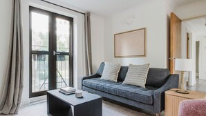 Een moderne woonkamer met een grijze bank, een zwarte salontafel, een roze fauteuil en een houten bijzettafeltje met een lamp.