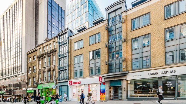 Een straat met moderne gebouwen, een café genaamd 'URBAN BARISTAS', en een winkel met de naam 'FIXNOLGY'.