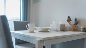 A minimalist dining area with a white table, a white cup, a bowl, a tissue box, and a small plant arrangement. - New 1 bedroom micro apartment for 2 (Wynnum)