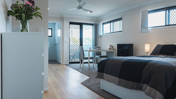 A bedroom with a bed, bedside tables, a desk, and a chair. - New 1 bedroom micro apartment for 2 (Wynnum)