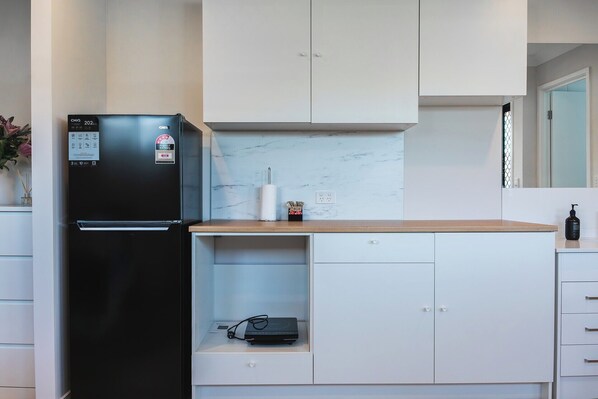 Una cocina moderna con un refrigerador negro, gabinetes blancos y un protector contra salpicaduras de mármol.