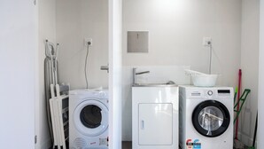 A laundry room with two front-loading washing machines, a small utility cabinet, and a mop on the floor. - New 1 bedroom micro apartment for 2 (Wynnum)