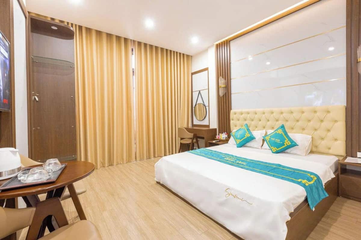 A hotel room with a large bed, a desk, a chair, and a TV.