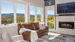 A modern living room with a large window, a fireplace, and a mounted television.