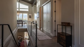 A spacious interior with a high ceiling, a staircase leading to an upper level, a dining area with a view, and a large wardrobe.