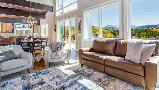 A spacious living area with a large window offering a mountain view, a cozy seating arrangement, and a modern kitchen in the background.