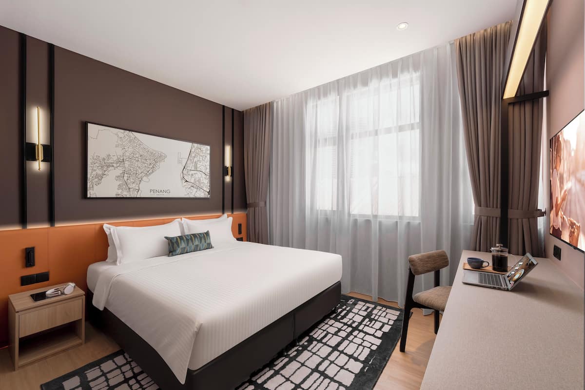 Una camera d'hotel moderna con un letto grande, una scrivania con un portatile, una mappa appesa al muro e vista sulla città attraverso tende leggere.