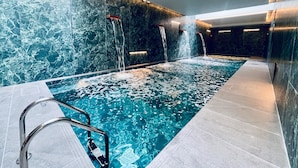 Ein Innenpool mit mehreren Wasserstrahlen, umgeben von Marmorwänden und modernem Design.