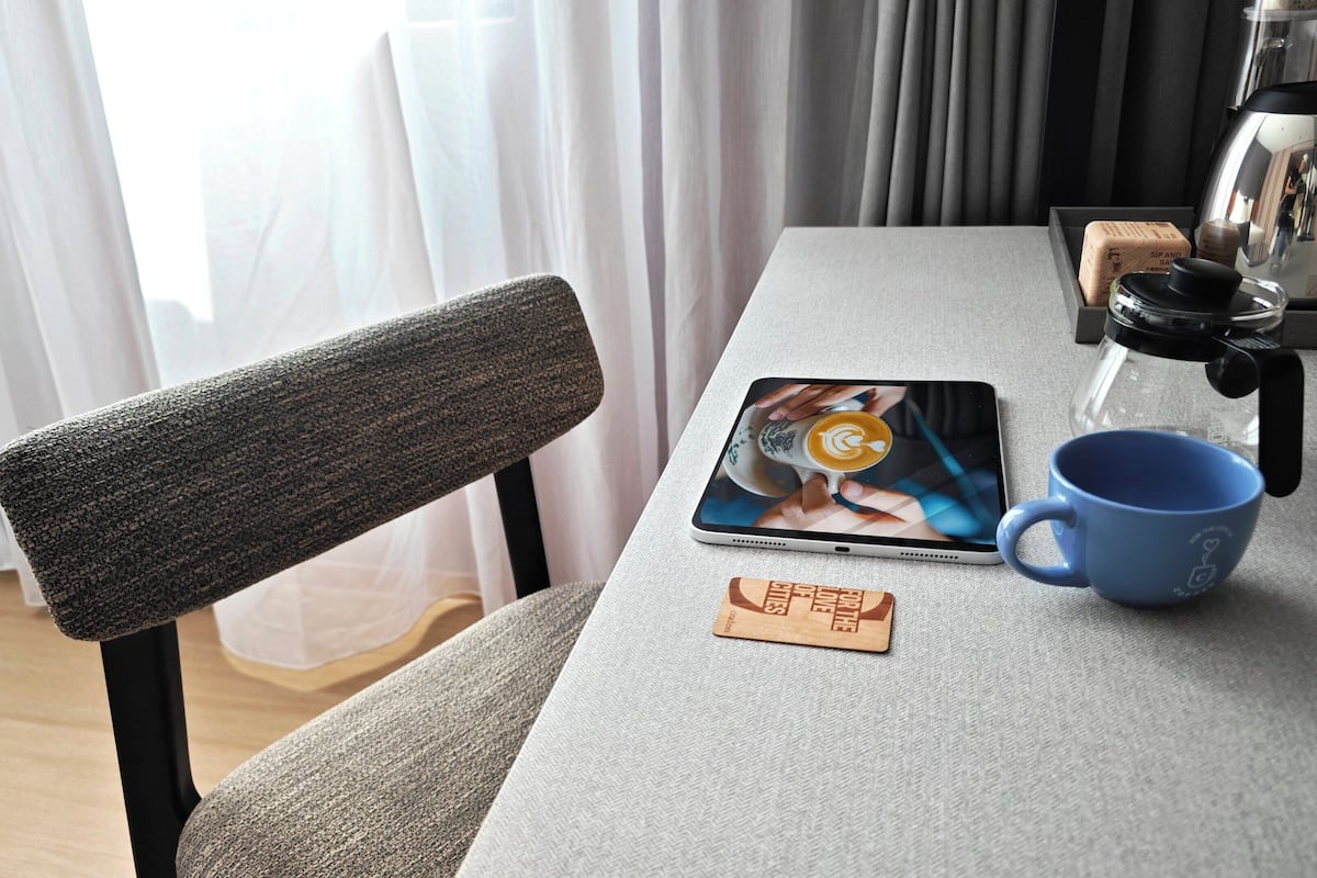 Un tavolo con un tablet che mostra una tazza da caffè, una mug blu, un sottobicchiere di legno e una macchina per il caffè.