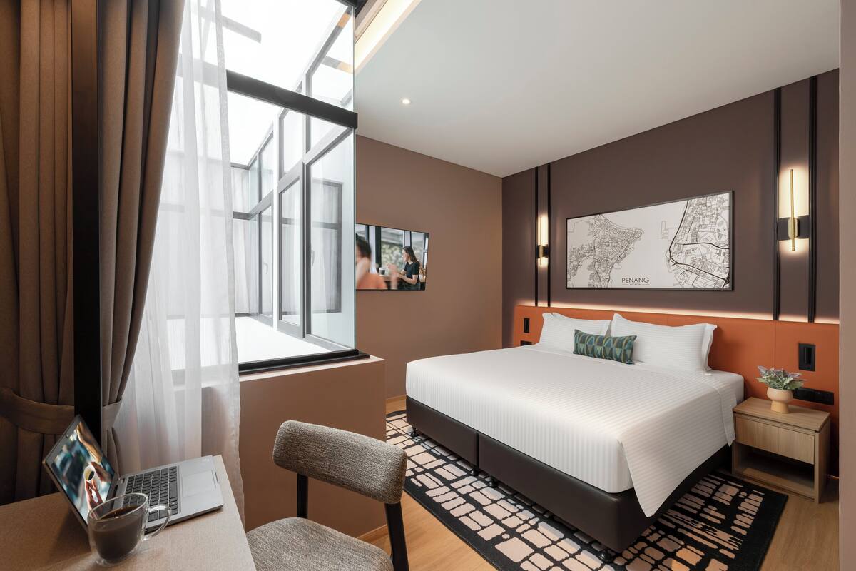 Una camera d'hotel moderna con un letto grande, una scrivania con un portatile, una tazza da caffè e una mappa appesa al muro.