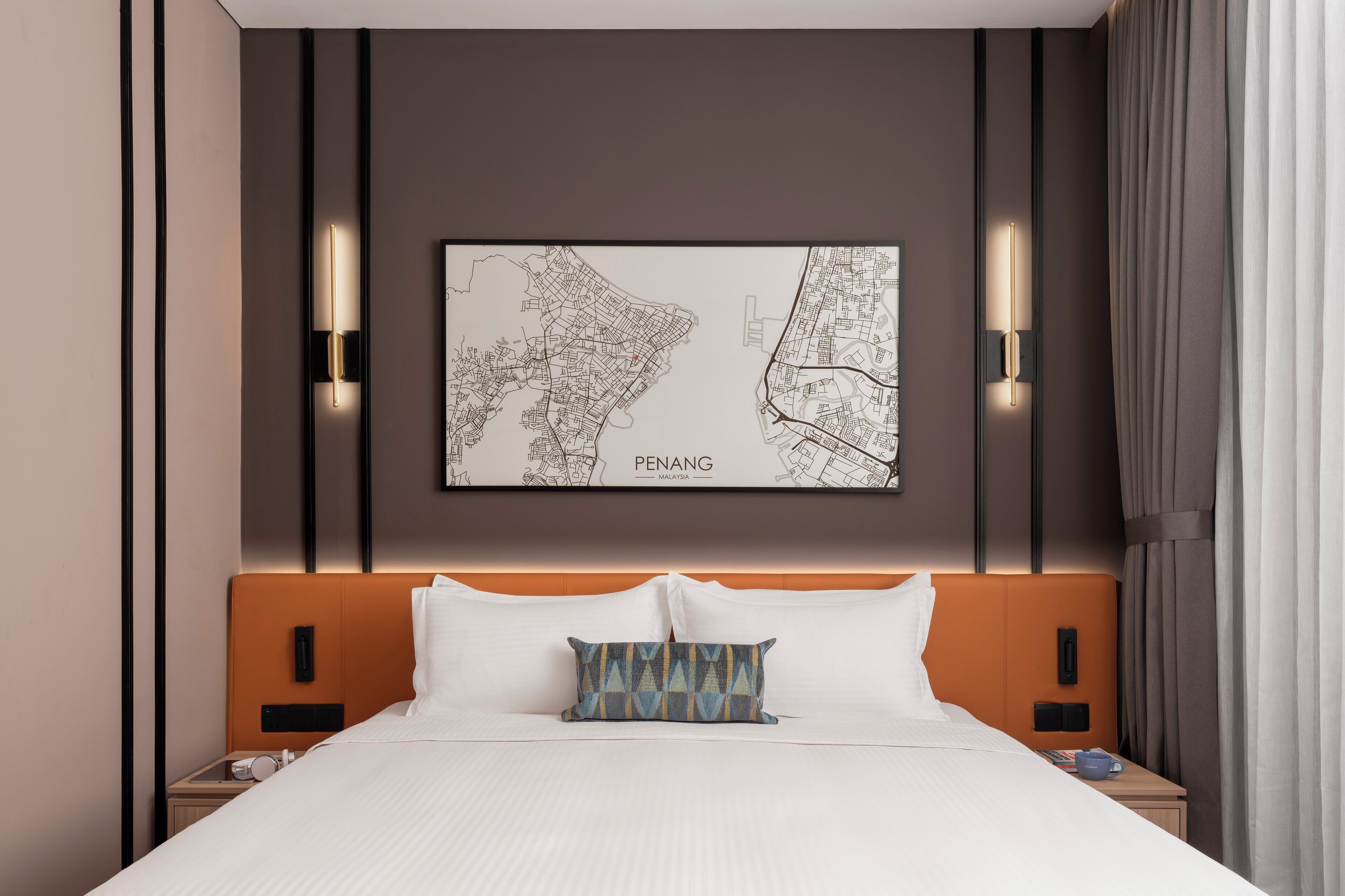 A hotel room with a large bed, a headboard, two bedside tables, a wall-mounted map, and two wall sconces.