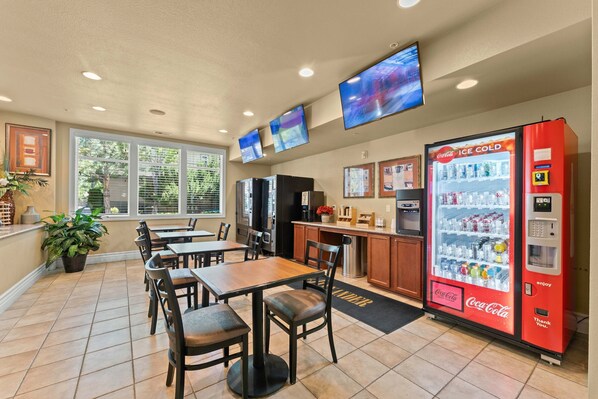 Un restaurante con mesas y sillas, una máquina expendedora de Coca-Cola y una zona de cocina.