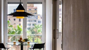 Un coin repas avec une table ronde en verre, deux chaises noires, un saladier de fruits et un verre de jus d’orange.