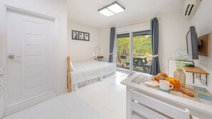 Un dormitorio con una cama, una mesita de noche con una taza y pasteles, un televisor y vistas a un patio exterior.