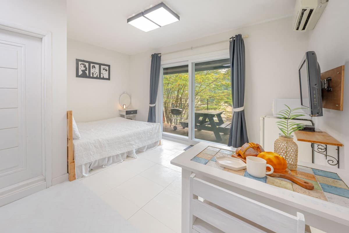 A bedroom with a bed, a bedside table with a cup and pastries, a TV, and a view of an outdoor patio.