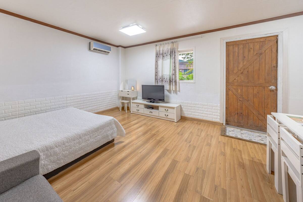 A bedroom with a bed, a TV, a dresser, and a wooden door.