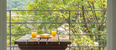 Ein Tisch mit einem Glas Orangensaft und einer Toastplatte, vor einem Fenster mit Blick auf Bäume.