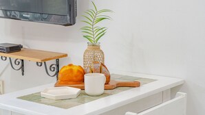 Una encimera de cocina con un proyector, un jarrón tejido con una planta, un panecillo, una taza blanca y una tabla de cortar.