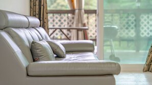 Un sofá de cuero blanco con cojines, ubicado cerca de un ventanal corredero que da a un patio exterior.