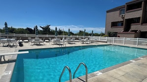 A swimming pool with lounge chairs and umbrellas, surrounded by a white fence and trees. - Brigantine Breeze 2-BR Coastal Retreat Steps to Beach (Brigantine)