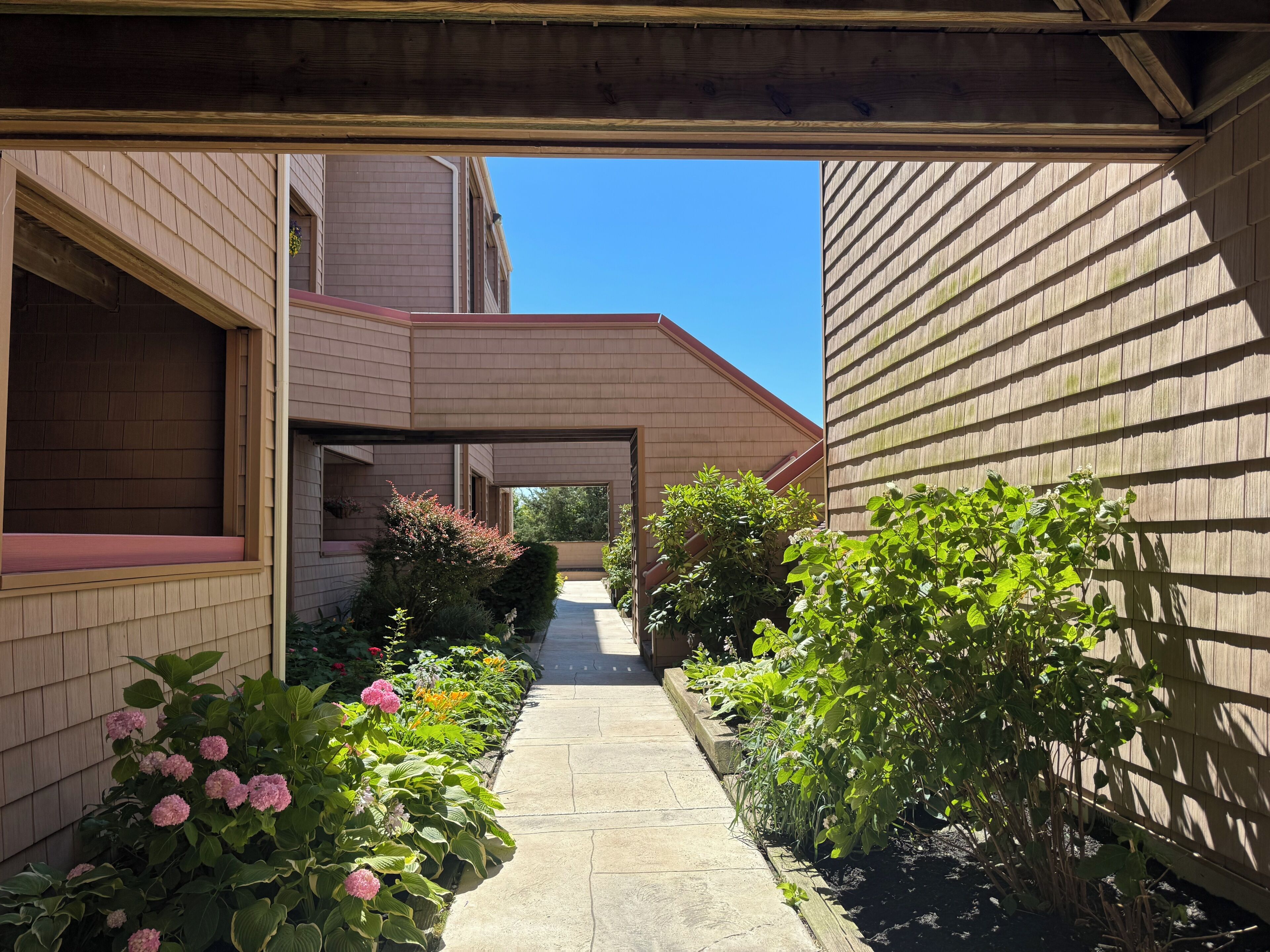 A narrow pathway flanked by buildings with wooden siding and brick walls, leading to a covered area.